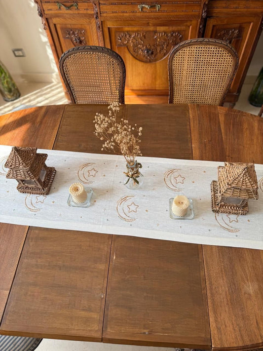 Wooden dining table with a decorative runner, candles, and wicker chairs. ramadan decoration زينة رمضان للبيت